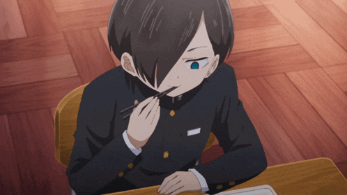 a boy with black hair and a blue eye is sitting at a desk with chopsticks in his mouth