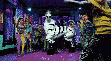 a group of people are dancing in a room with a zebra mascot in the middle