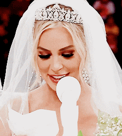the bride is wearing a tiara and veil and is holding a microphone