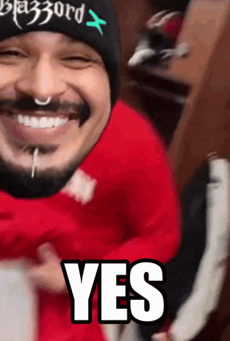 a man with a beard wearing a red shirt and a black hat says yes