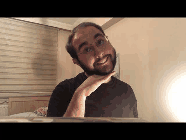 a man with glasses and a beard is sitting in front of a laptop computer .