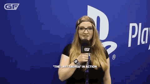 a woman with glasses is holding a microphone in front of a playstation sign .