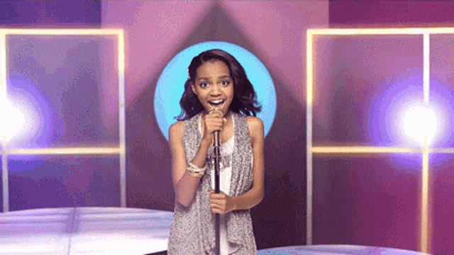 a woman is singing into a microphone in front of a purple background
