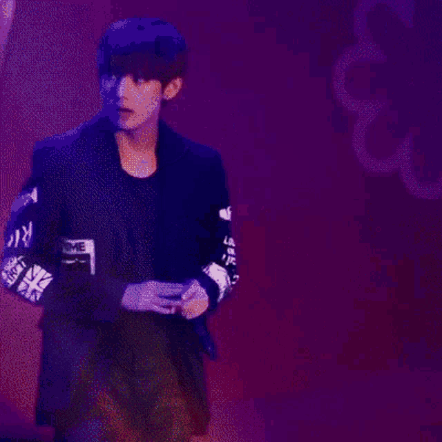 a man in a black jacket is standing in front of a red background with smoke coming out of it .