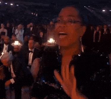 a woman in a black dress and glasses is applauding in front of a crowd of people .