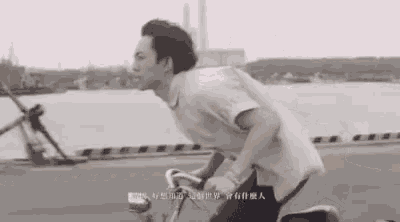 a man is riding a bicycle down a street near a body of water .