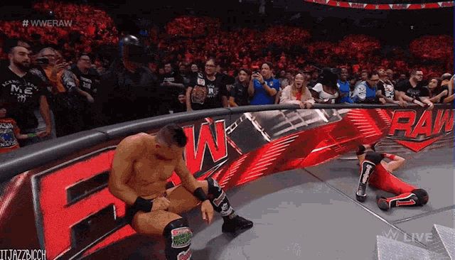a man sits on the edge of a wrestling ring next to a sign that says raw