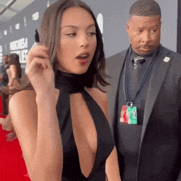 a man in a suit stands next to a woman in a black dress with a plunging neckline