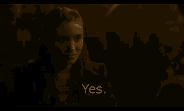 a woman is sitting in a dark room talking to someone and the words yes are visible .