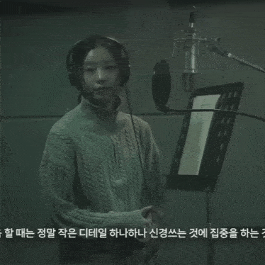 a woman wearing headphones stands in front of a microphone in a recording studio