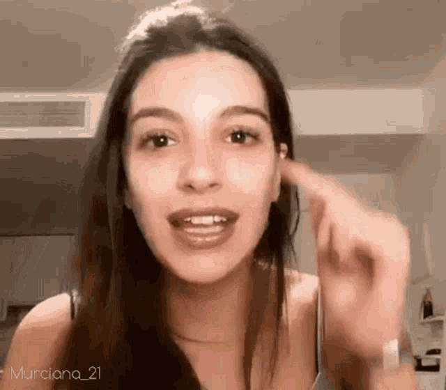 a woman is pointing her finger at her ear while talking to the camera .