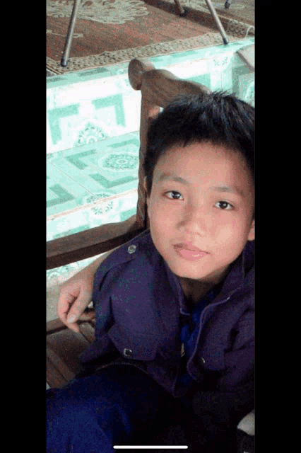 a young boy in a purple jacket is sitting on a chair