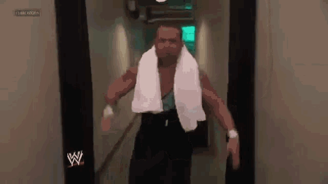 a wrestler is walking down a hallway with a white towel around his neck .