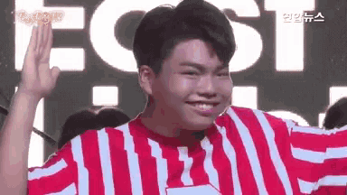 a young man wearing a red and white striped shirt is smiling and waving .