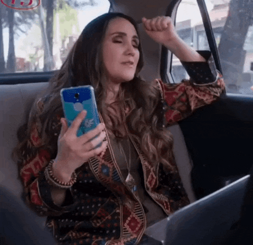 a woman is sitting in the back seat of a car while holding a cell phone .