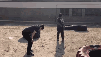 a man and a woman are doing exercises in a field with tires .