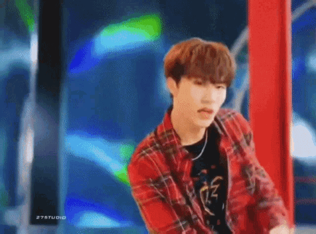a young man wearing a red plaid shirt and headphones is standing next to a pole .