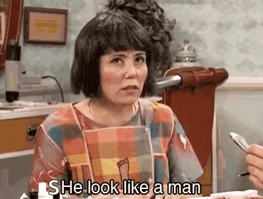 a woman in an apron is sitting at a table with a pen in her hand and says `` she look like a man '' .