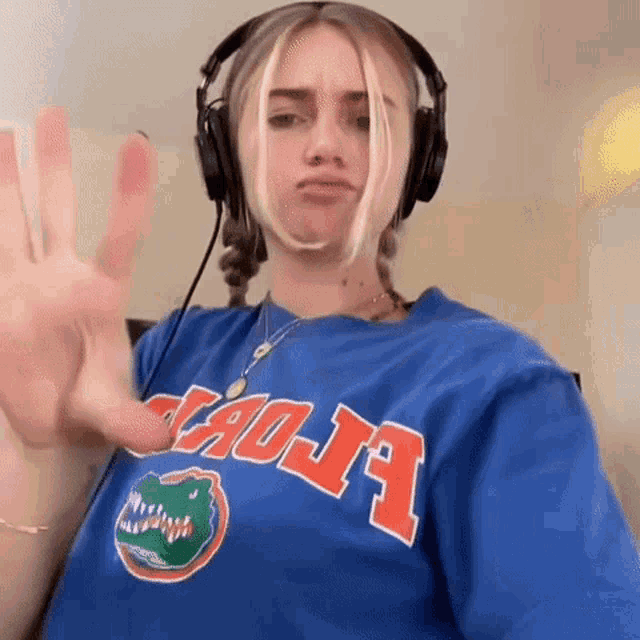 a woman wearing headphones and a blue t-shirt with a gator on it is making a funny face .