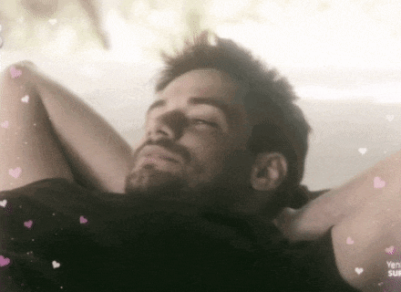 a man with a beard is laying down with his eyes closed and his arms behind his head .