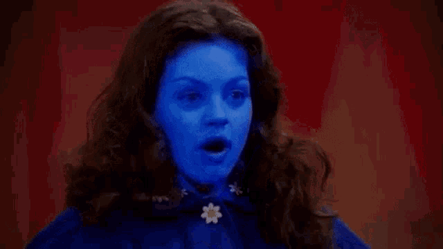 a woman with blue paint on her face is wearing a blue cape and earrings .