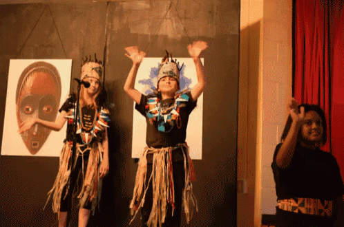 a group of children are dancing in front of a wall with a picture of an african mask on it
