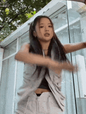 a woman in a grey vest and white pants is dancing in front of a glass door .