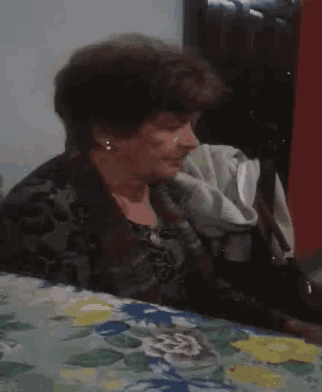 a woman is sitting at a table with a floral table cloth