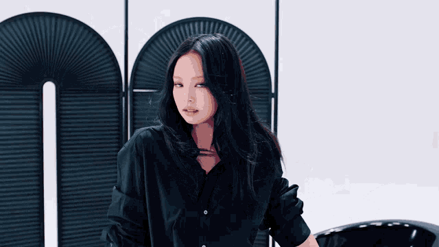 a woman in a black shirt is standing in front of a wall