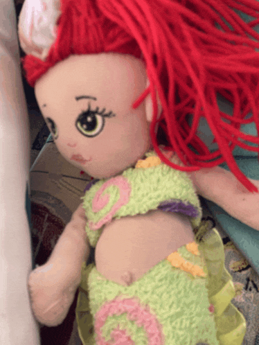 a stuffed doll with red hair is wearing a green and pink outfit