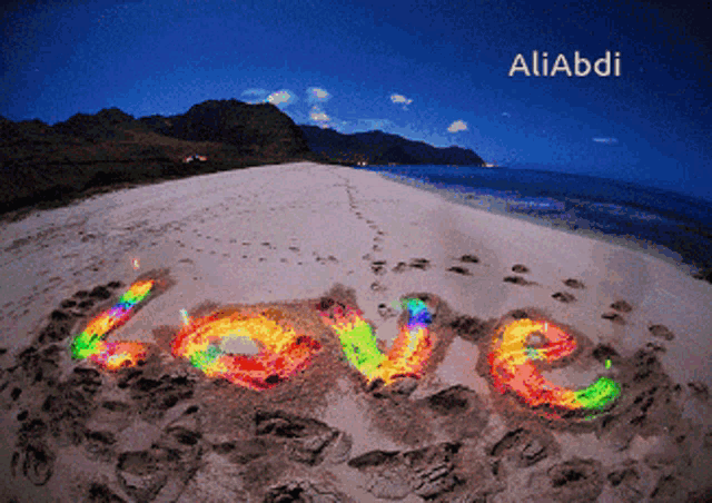 the word love is written in rainbow colors in the sand