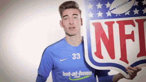 a man in a blue jersey with the number 33 on it holds up an nfl sign