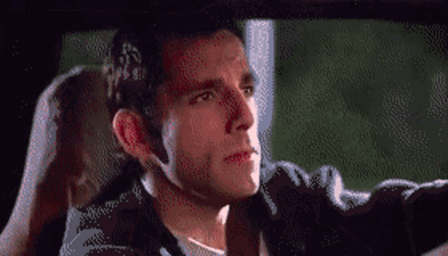 a man in a black jacket is driving a car and looking out the window