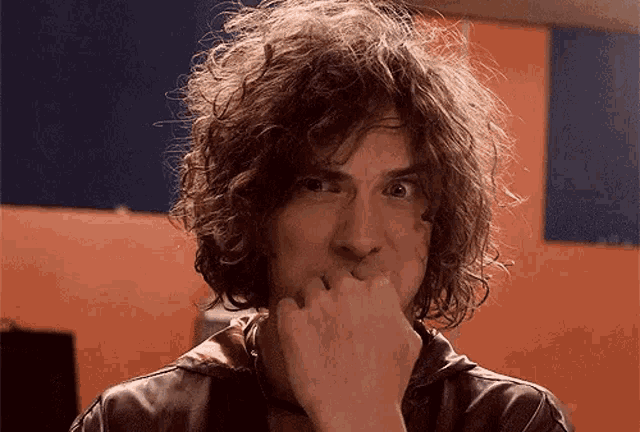 a man with curly hair is covering his mouth with his hand and looking at the camera .