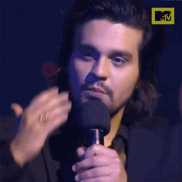 a close up of a man speaking into a microphone with a mtv logo behind him