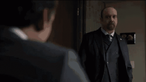a man in a suit and tie is standing next to another man in a room and says `` be creative '' .