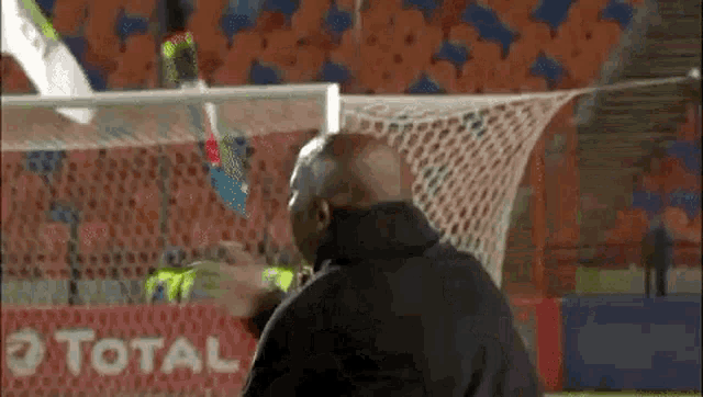 a man is standing in front of a soccer goal with a total sign in the background .