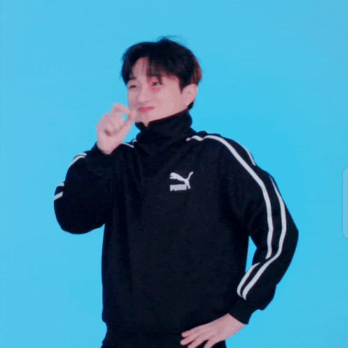 a man wearing a black puma jacket is making a heart shape with his finger