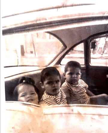 a black and white photo of three children sitting in the back seat of a car