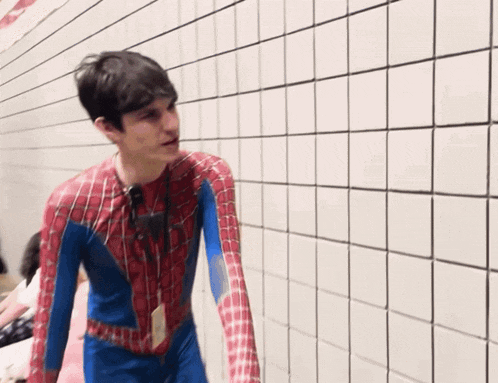 a man in a spiderman costume stands in front of a wall