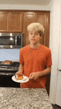 a young man in an orange shirt is holding a plate with a piece of food on it