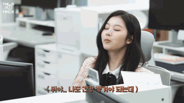 a woman sitting at a desk with her eyes closed and a twice logo on the bottom right