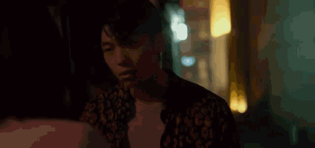 a man in a leopard print shirt is holding a piece of paper in his hand in a dark room .
