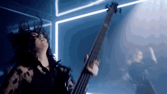 a woman playing a bass guitar in front of a blue light