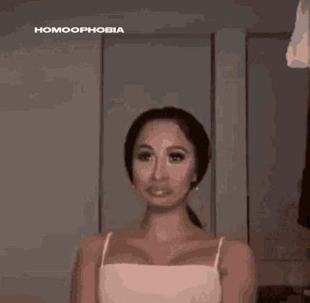 a woman in a white tank top is standing in front of a door and looking at the camera .