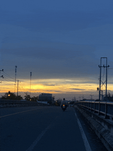a person riding a motorcycle down a road with a sunset in the background