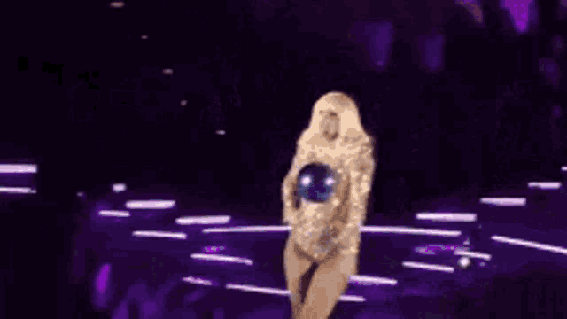 a woman is dancing on a stage in front of a crowd in a purple and gold outfit .