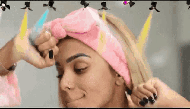 a woman wearing a pink headband is getting her hair done by a person .