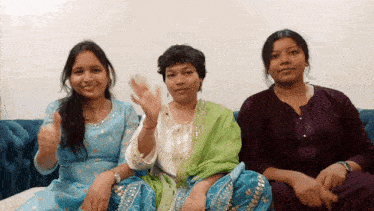 three women are sitting on a blue couch and one is waving