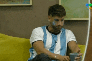 a man with blue paint on his face is sitting on a yellow couch holding a cup .